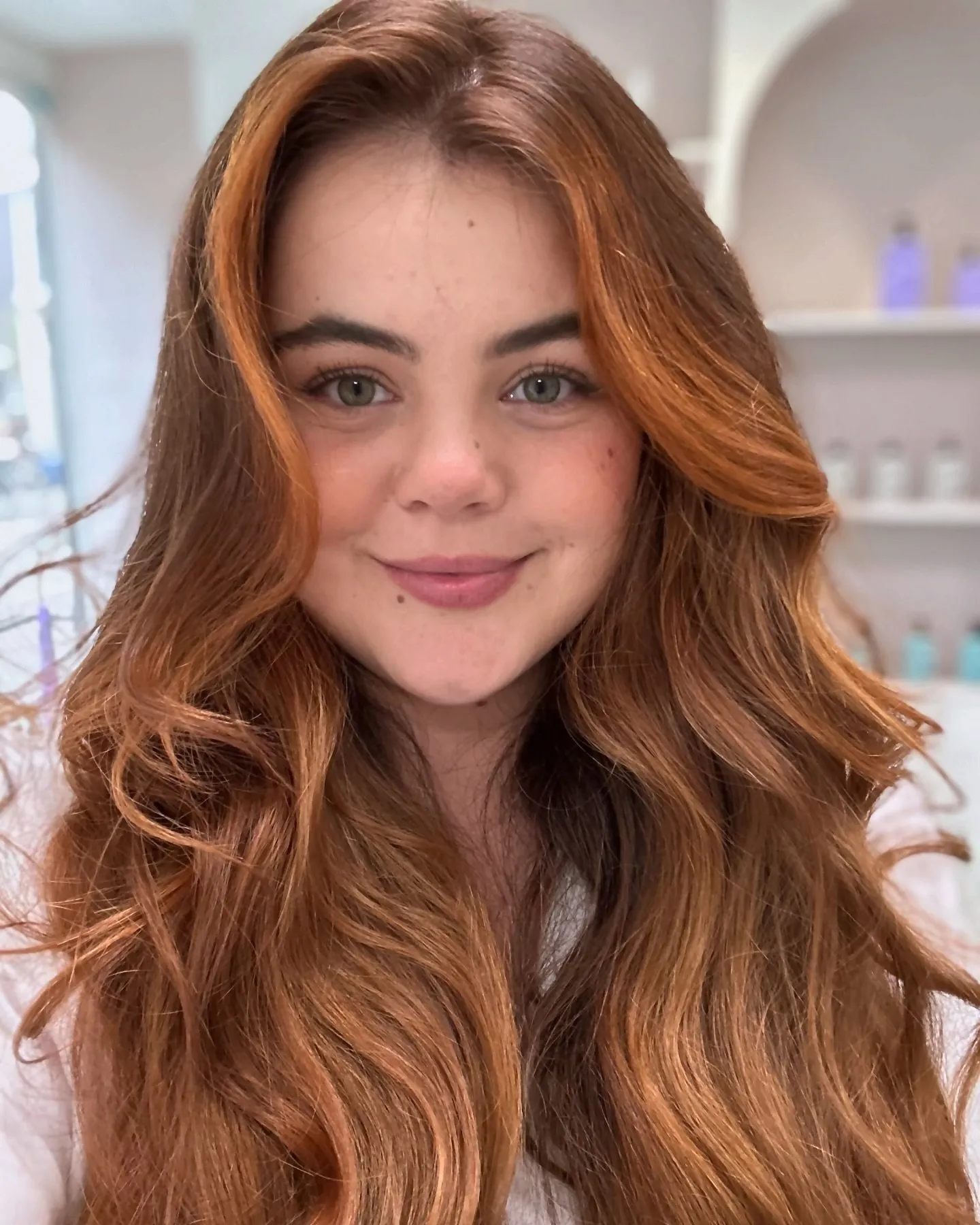 Vrouw met glanzend koperkleurig haar lacht in de salon