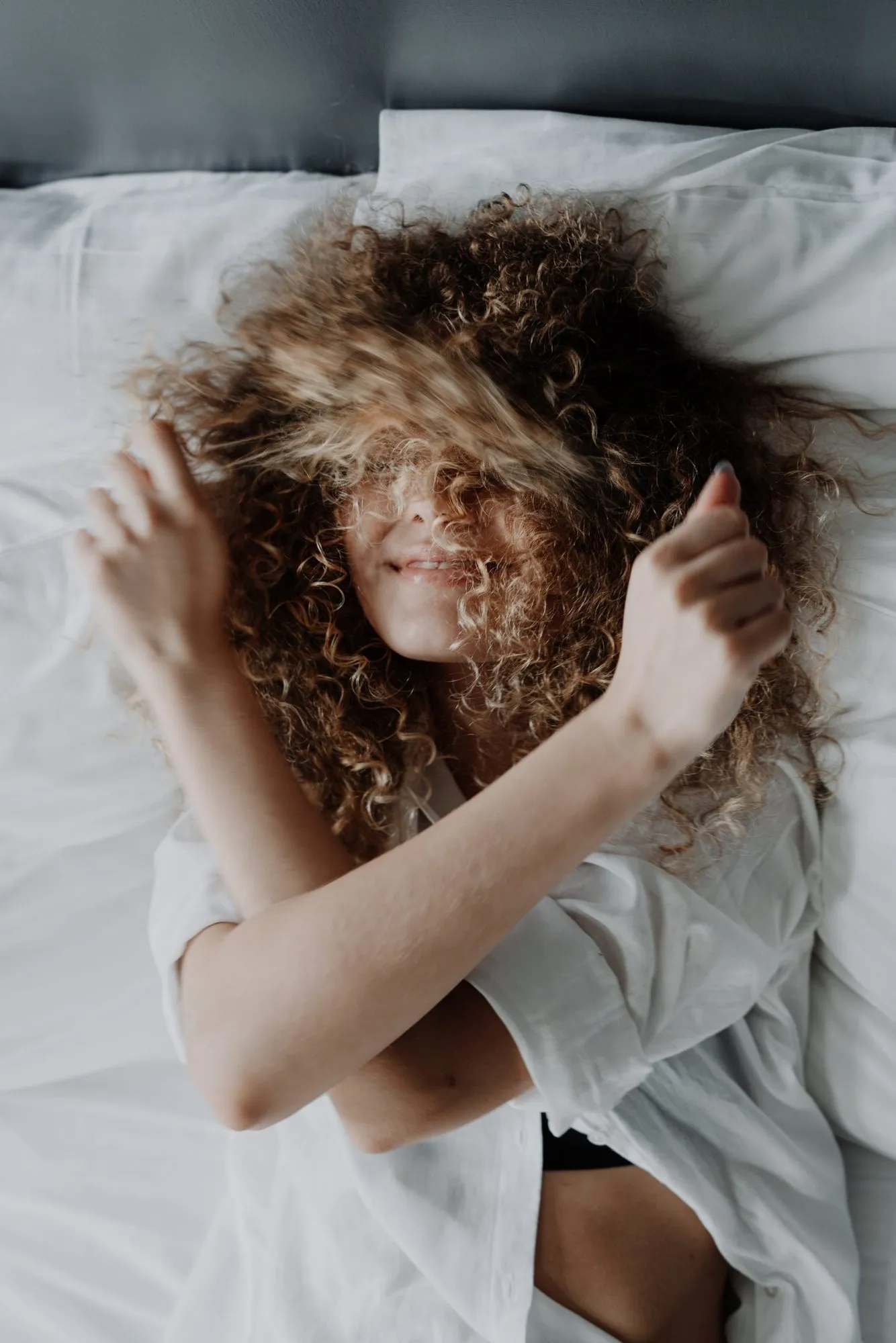 Vrouw met volle krullen op een wit bed
