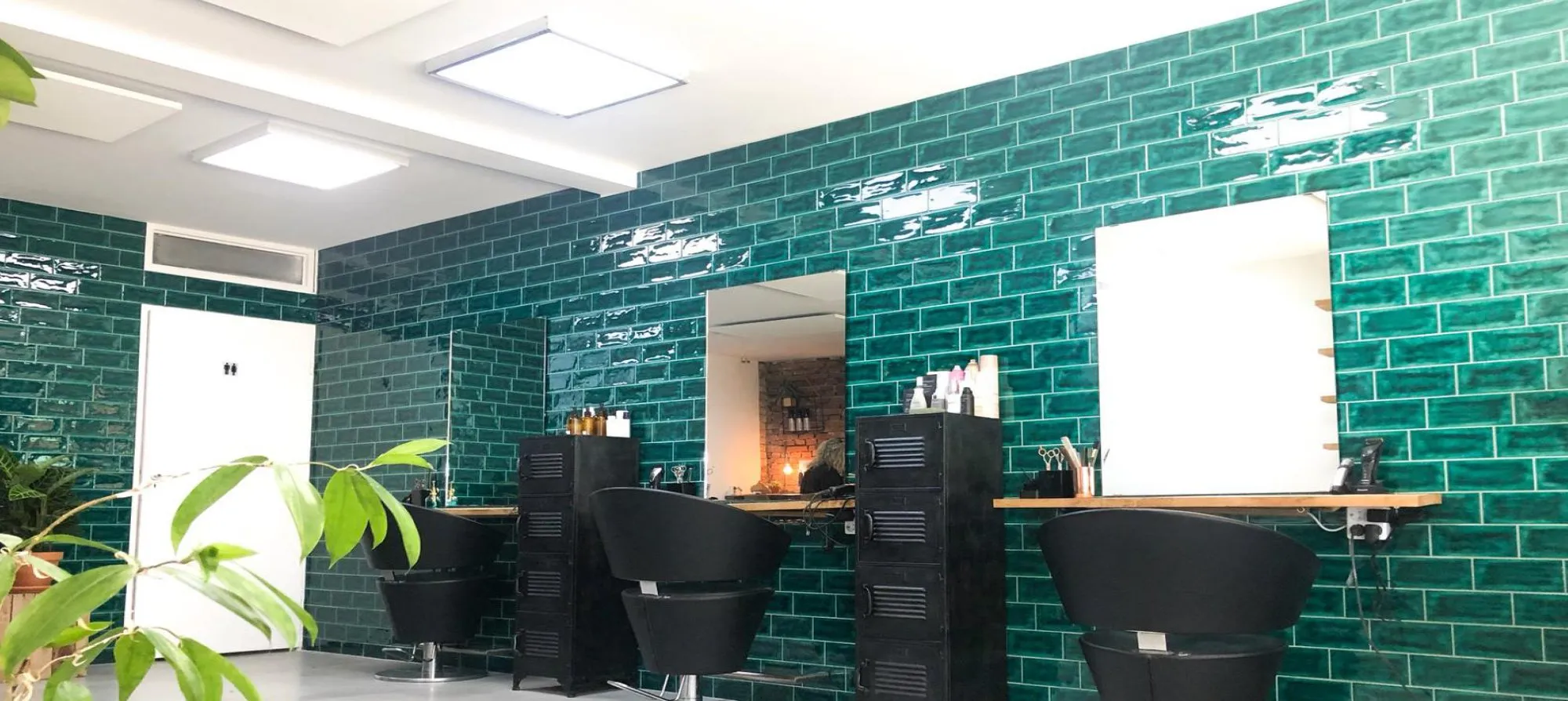 De salon van The Proof met een wand van groene tegels, zwarte stoelen en planten